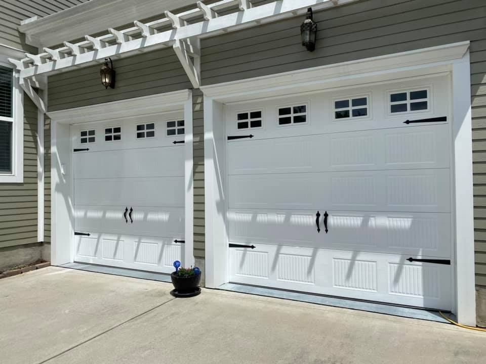 Two white garage doors with black hardware under a wooden pergola.