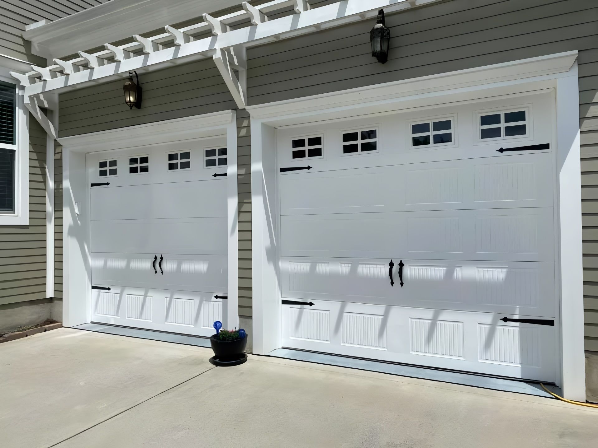 Two white garage doors with black hardware under a white pergola.