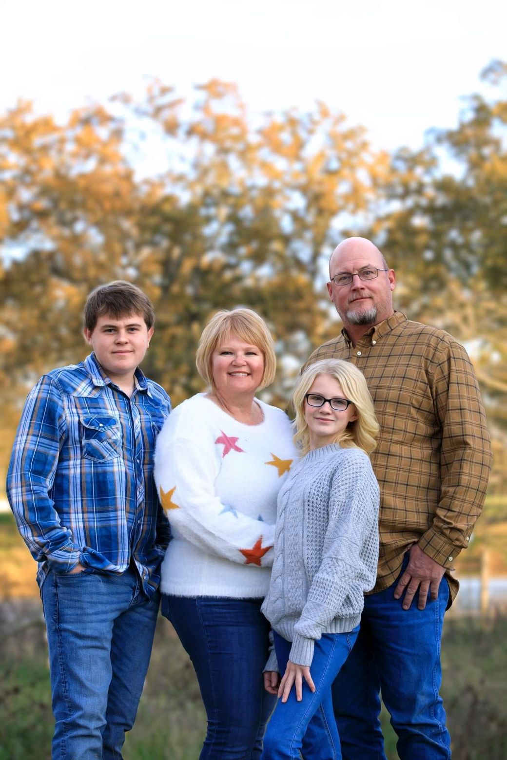 Four people standing outdoors in autumn, wearing casual clothes with colorful trees behind them.