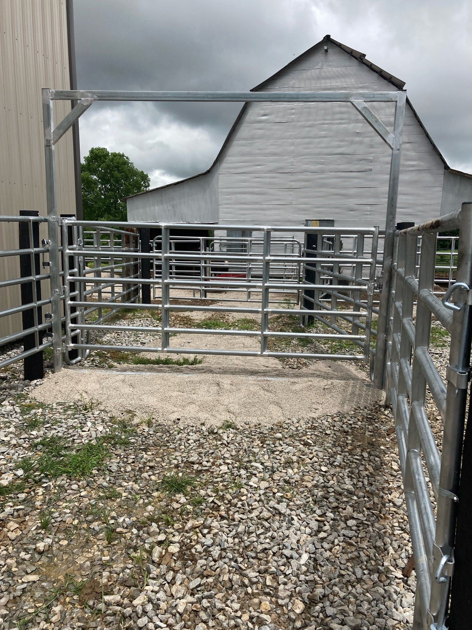 Gravel farm lane leading to a metal gate and silver barn under cloudy skies
