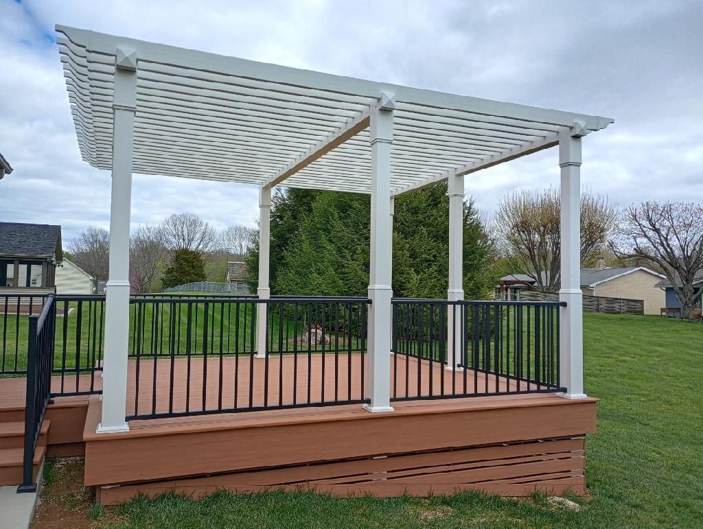 White pergola on a raised wooden deck with black railing in a grassy park.