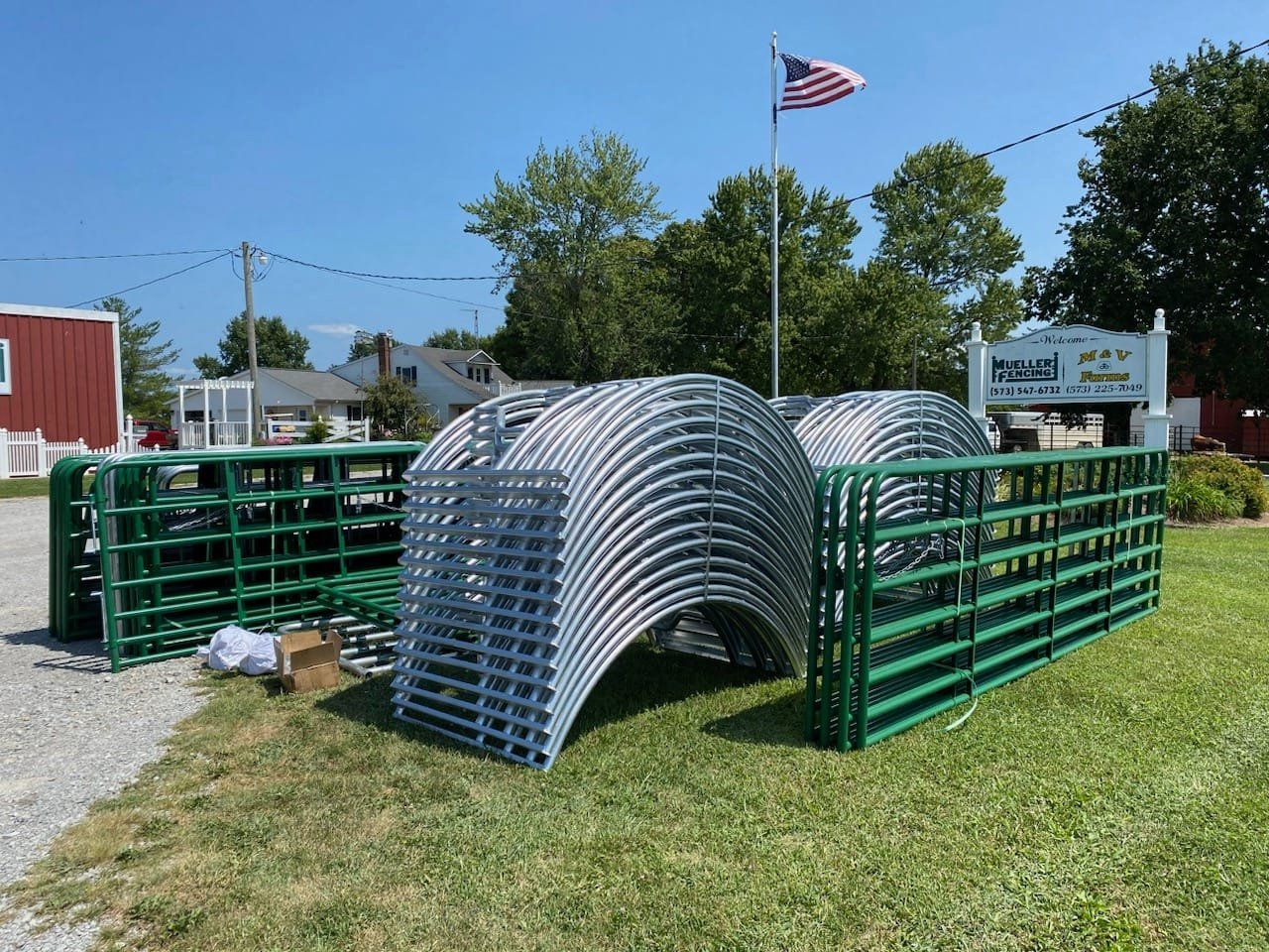 Stacked green and silver metal barricades on a grassy lot under a blue sky, with an American flag in the background