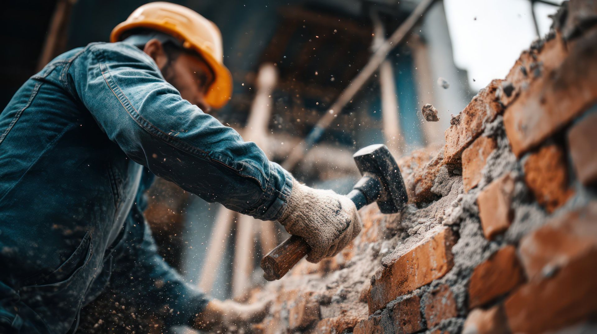 Construction worker in hard hat using a hammer to break a brick wall.