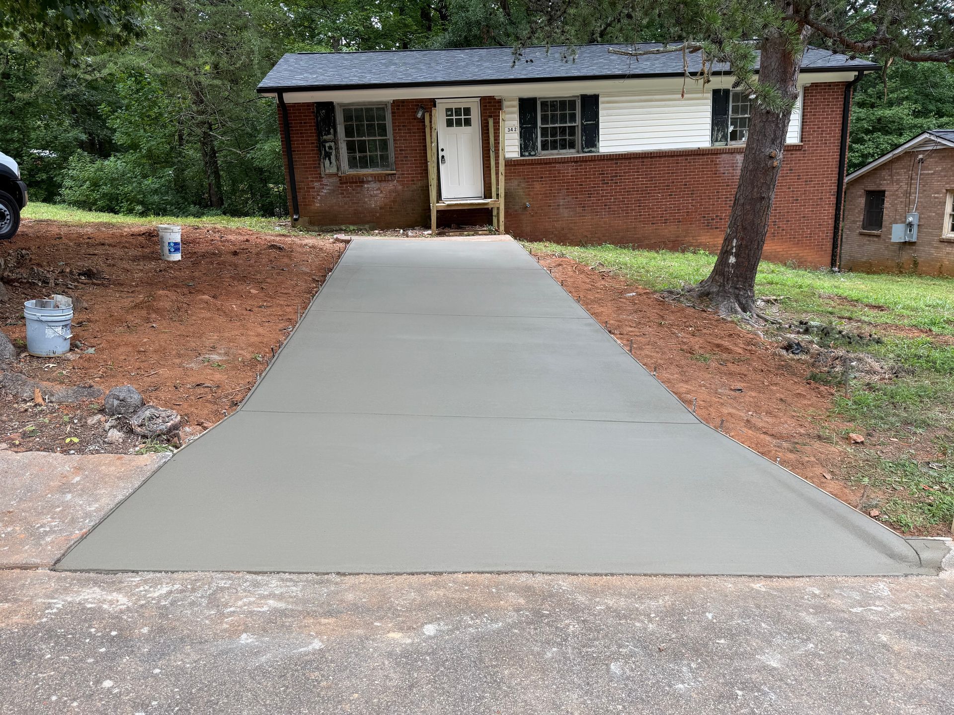 A house with a large concrete driveway and a basketball hoop. Blue sky, garage doors, and gravel landscaping.