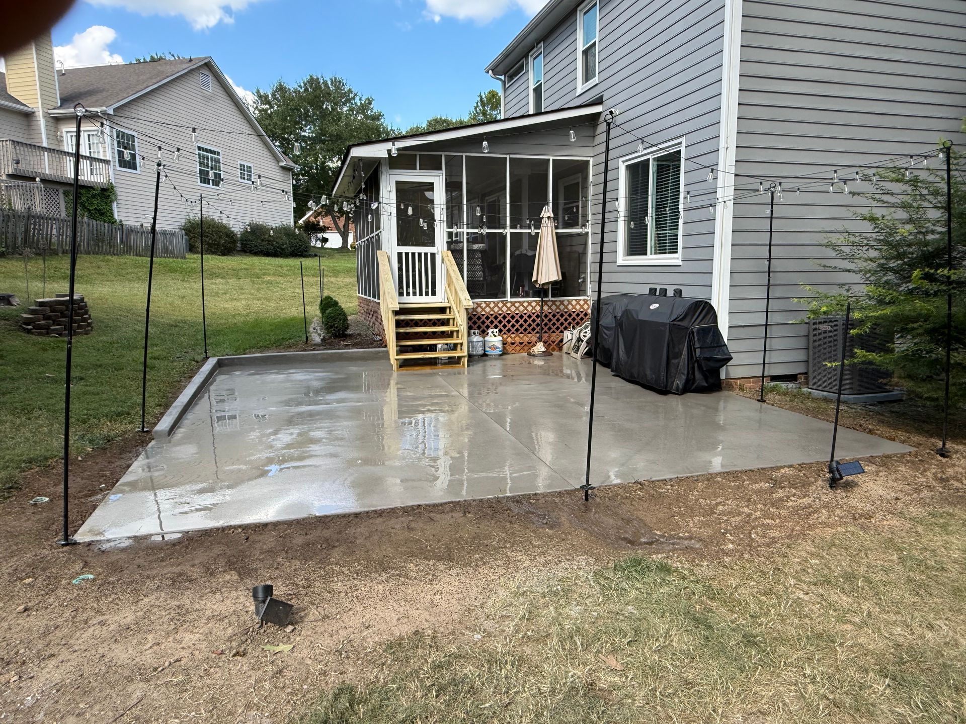 Patio with dining set and potted plants, overlooking a lush garden on a sunny day.