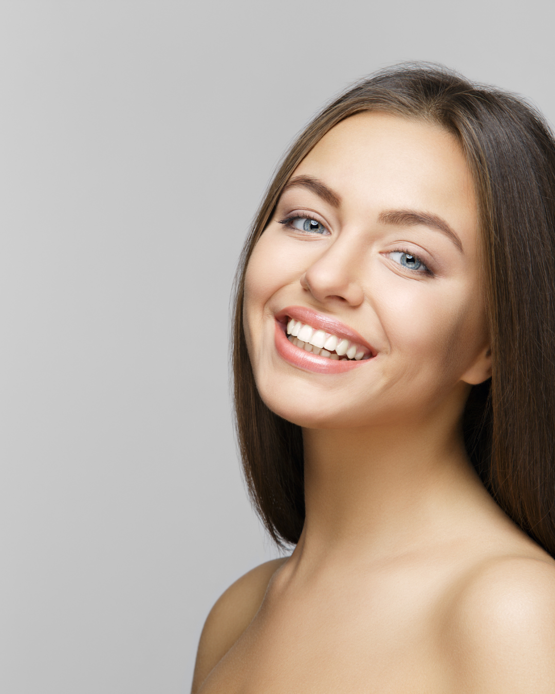 Femme souriante, regardant l'objectif, sur fond gris clair.