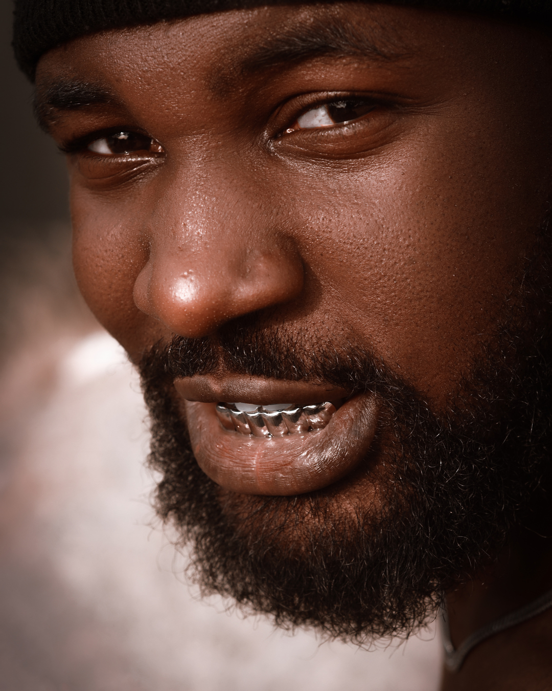 Gros plan sur une personne au teint foncé, barbue et aux dents grillagées ; souriante.