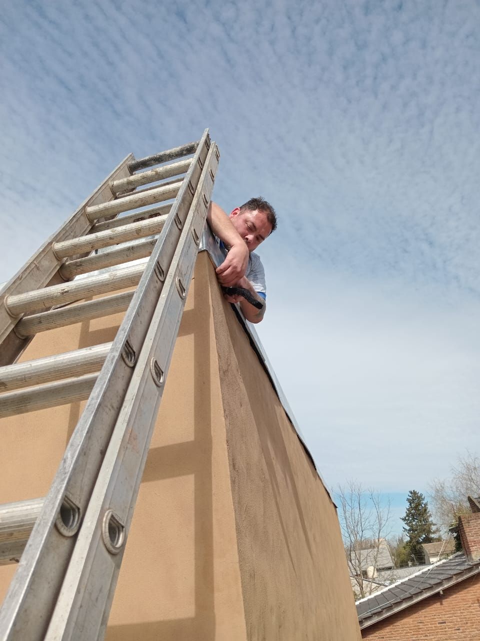 Un hombre está inclinado sobre una escalera en el costado de un edificio.