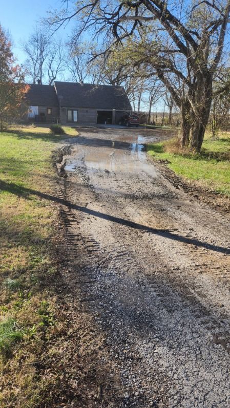 A dirt road leading to a house in the middle of a field.