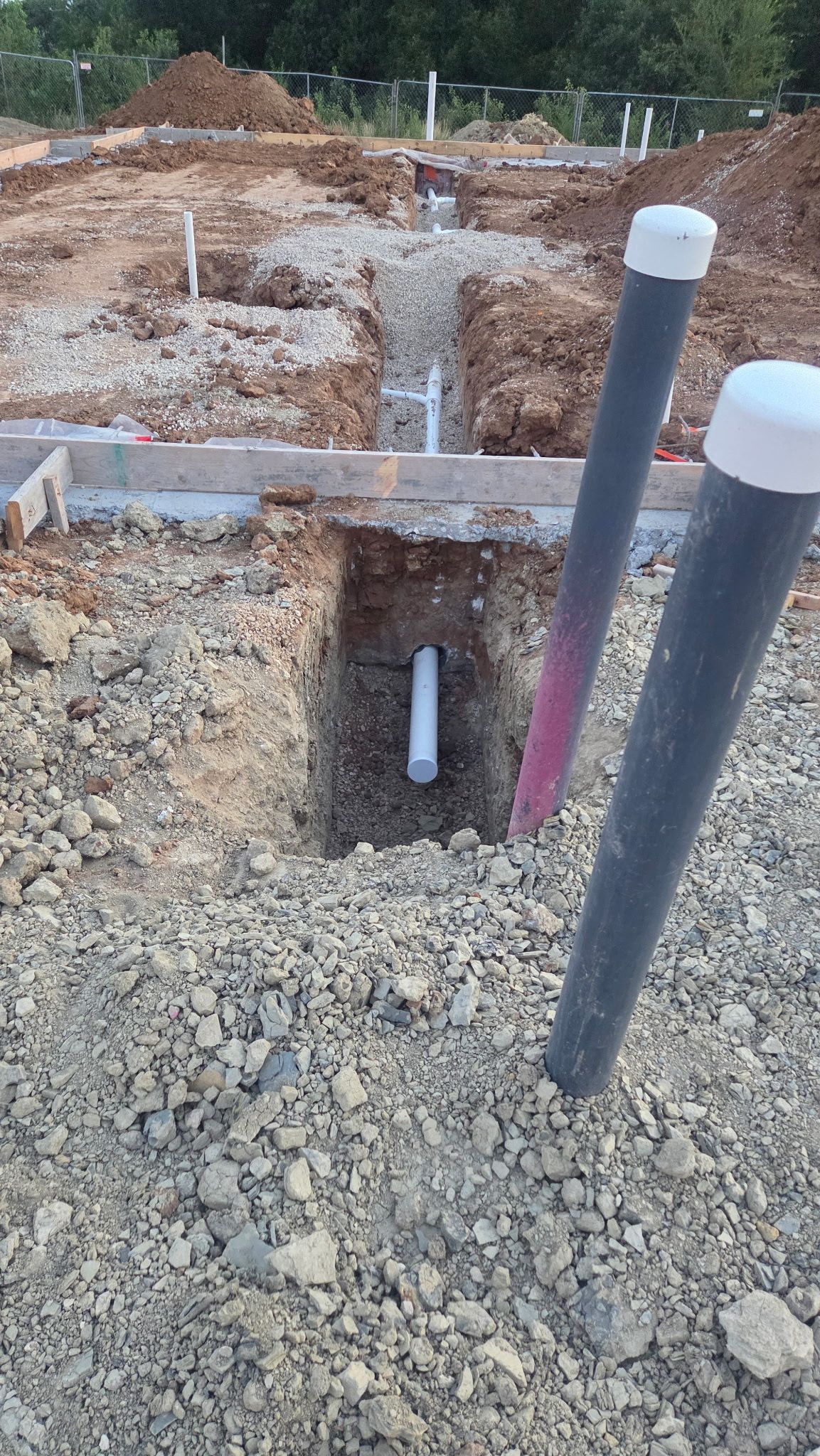 White PVC pipes in a trench on a construction site; concrete and exposed rebar are visible.