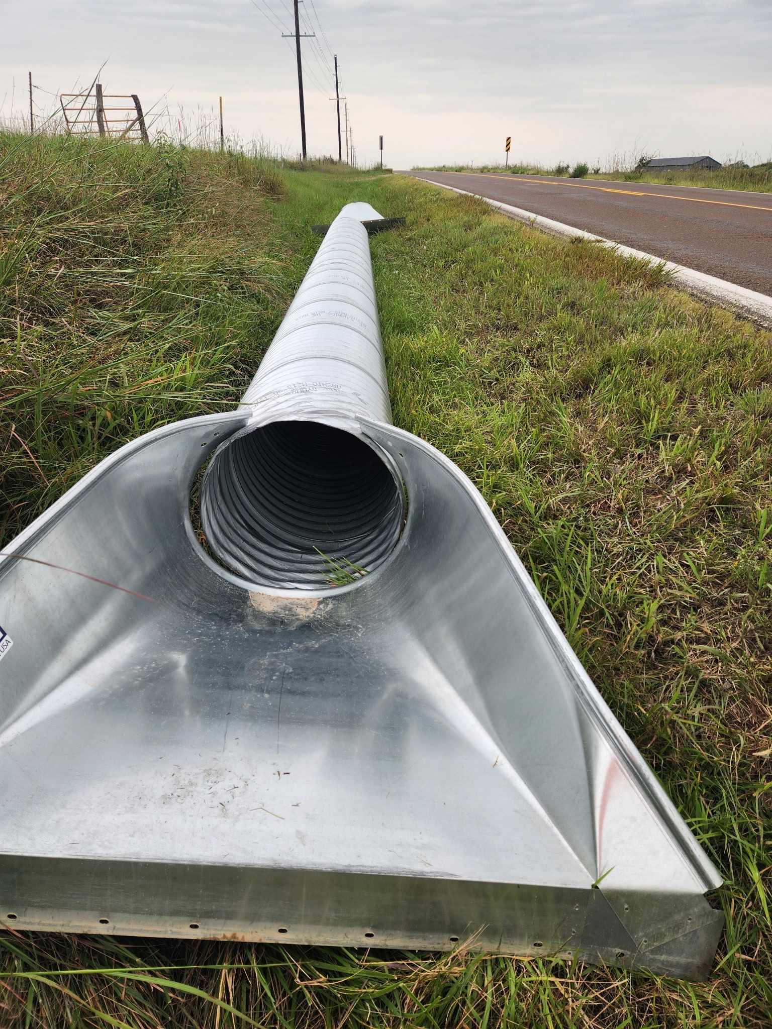 Excavator digging trench on a sunny day next to a building; operator inside the cab.