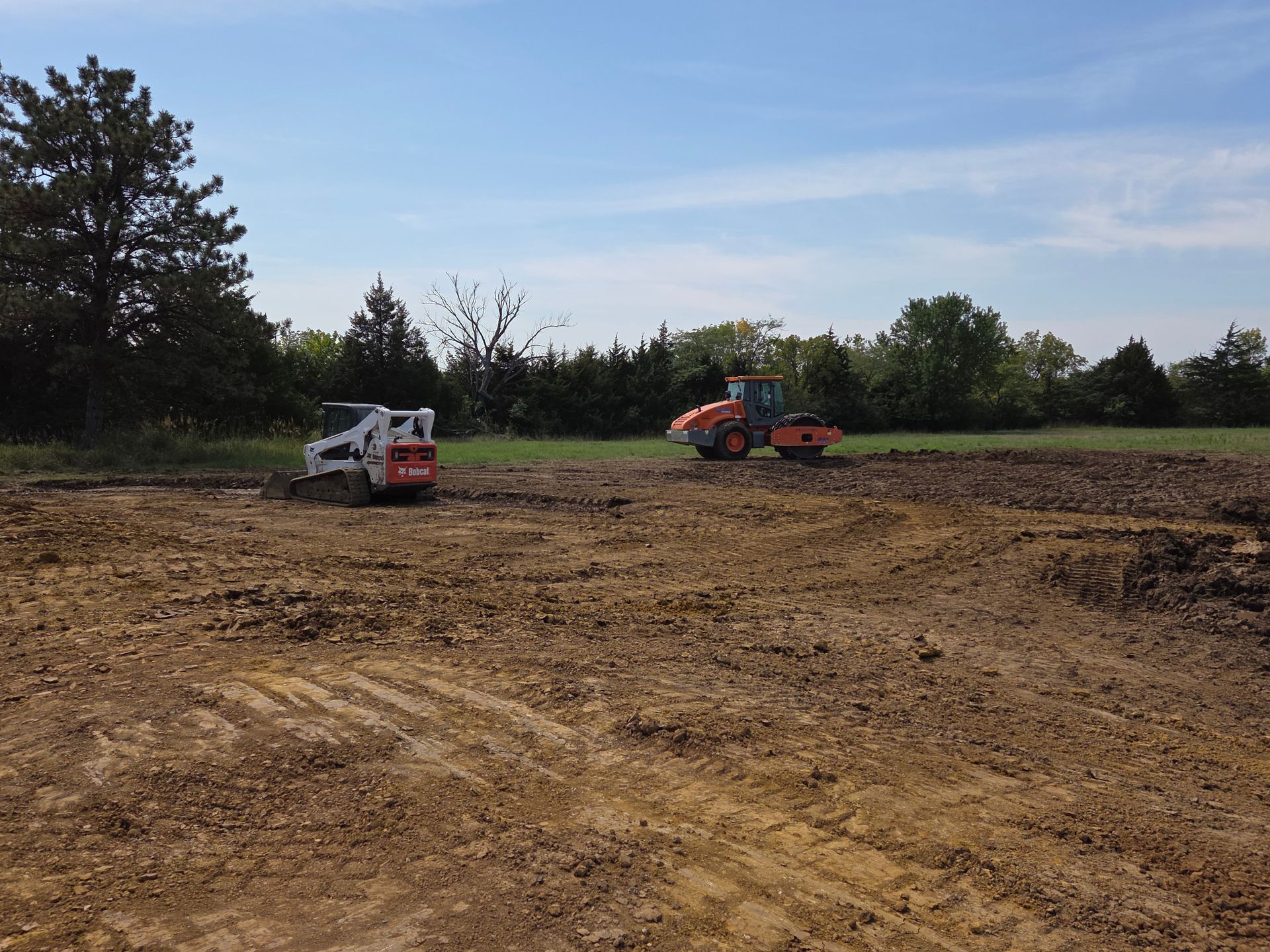 Brown earth in a field with a pile of dark soil and trees under a cloudy blue sky.