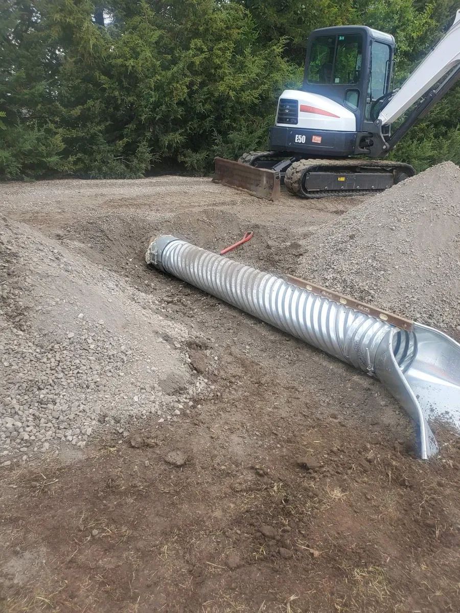 A bulldozer is digging a hole in the dirt next to a metal pipe.