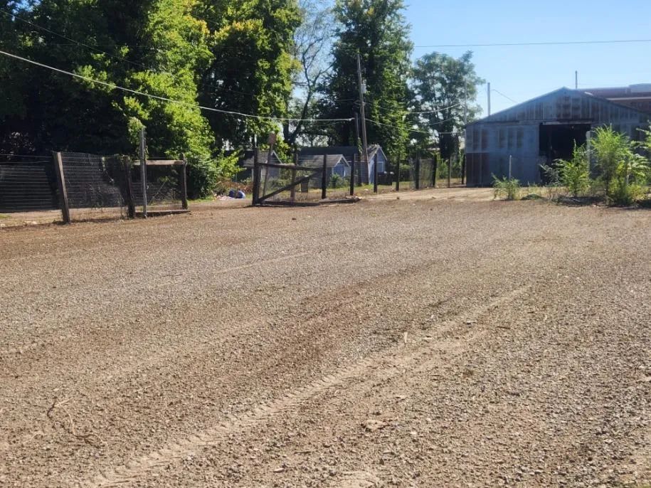 A dirt road with a fence and a building in the background
