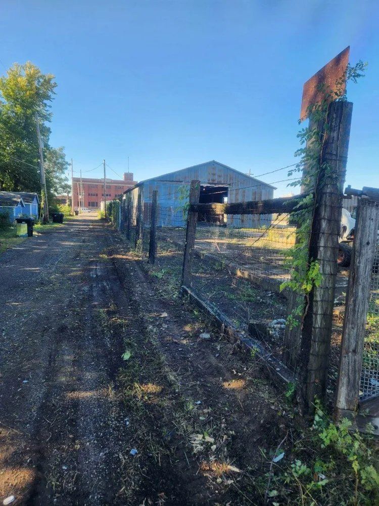 A dirt road with a fence and a building in the background
