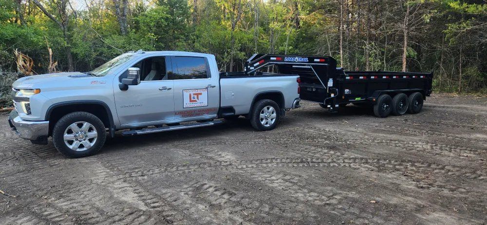 A white truck is towing a dump trailer in a dirt lot.