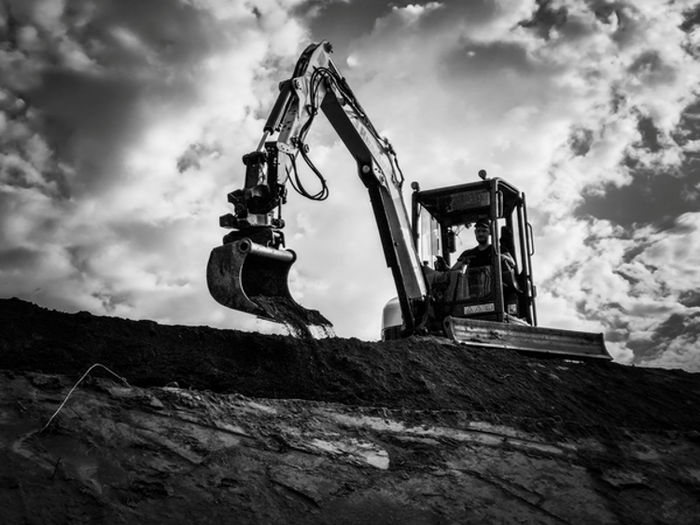 A small orange excavator is working on a construction site.