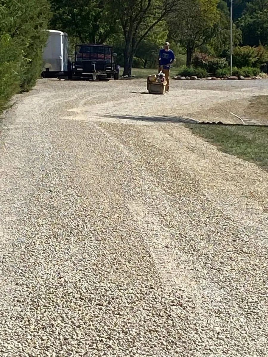 A man is driving a tractor down a gravel road.