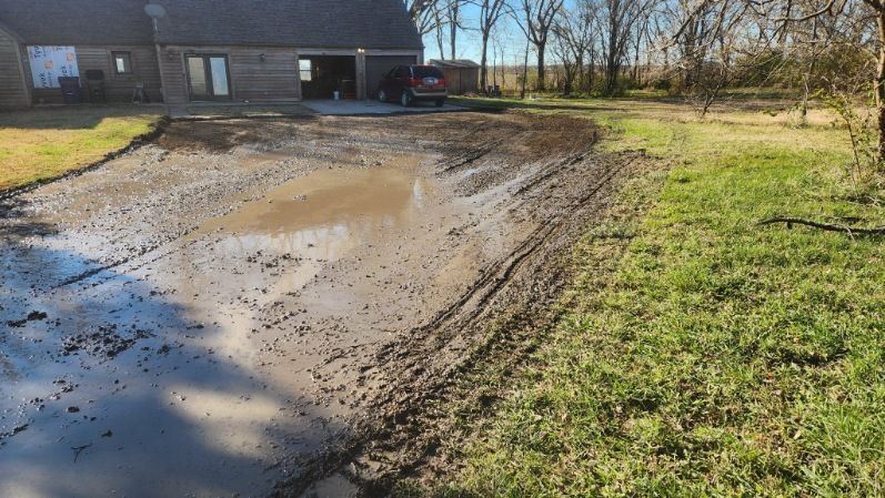 A car is parked in a muddy driveway in front of a house.