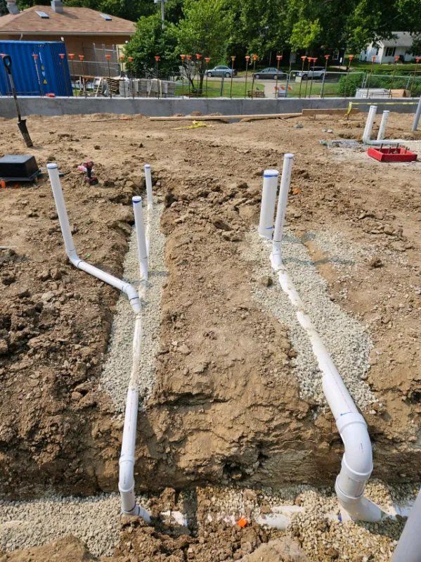 A bunch of pipes are laying in the dirt on a construction site.