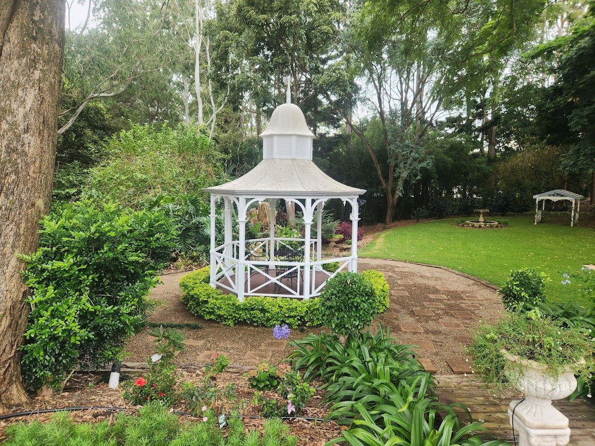 A white gazebo is sitting in the middle of a garden surrounded by trees.