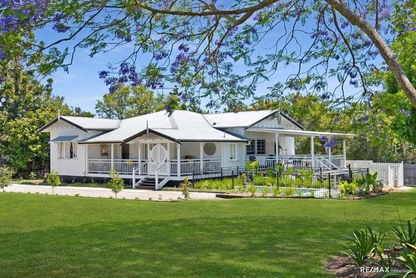 A large white house with a porch is surrounded by trees and grass — Painter In Sunshine Coast, QLD