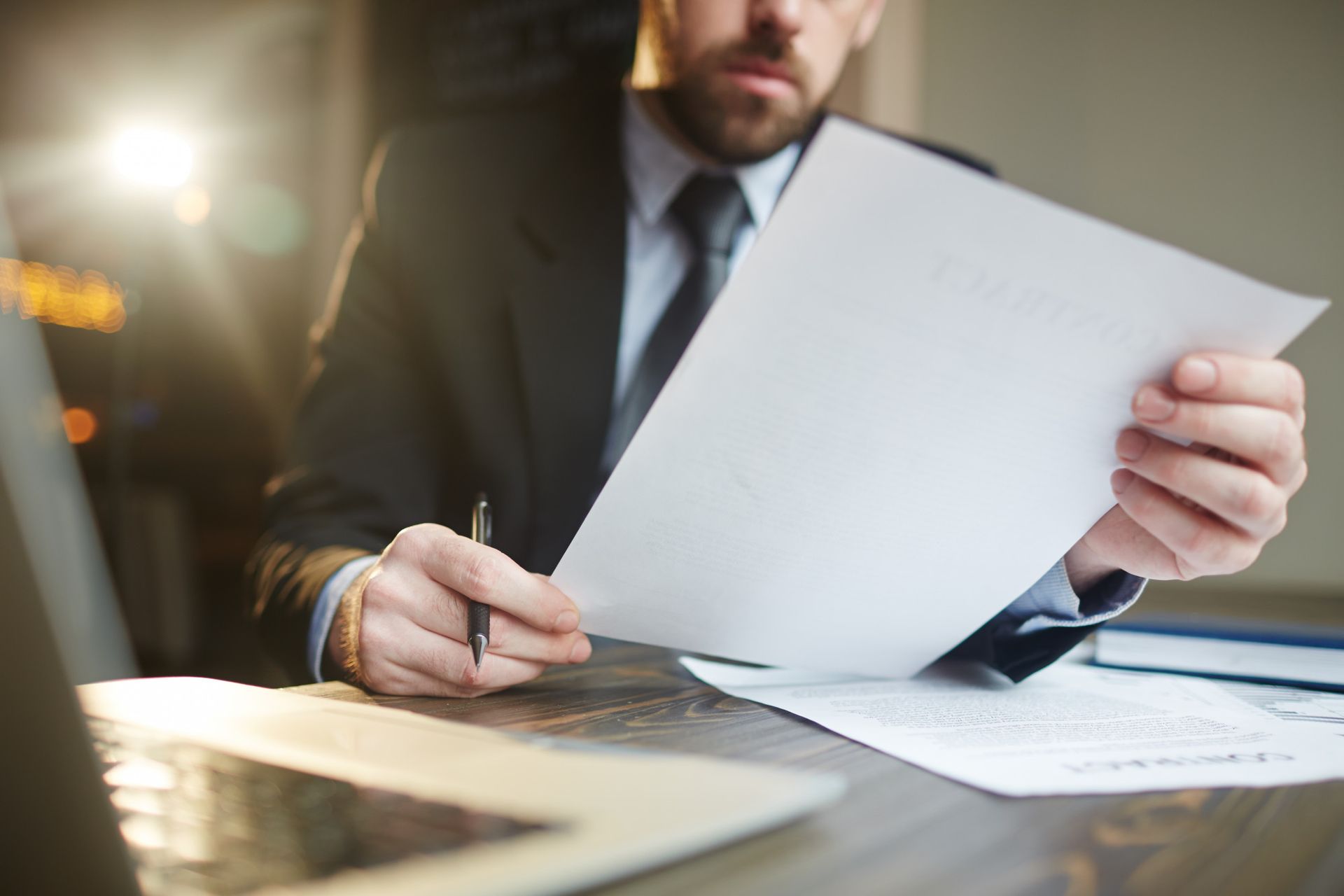 A man in a suit and tie is sitting at a desk holding a piece of paper and writing on it.