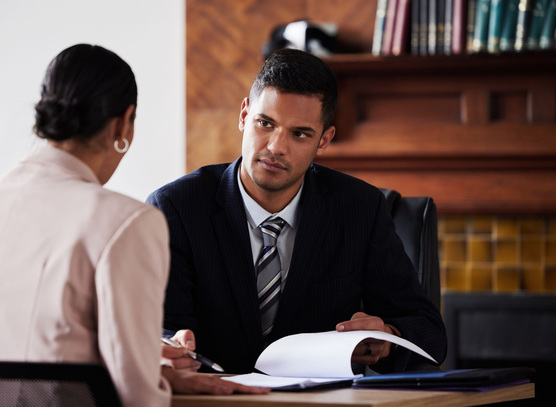 A man in a suit and tie is sitting at a table talking to a woman.