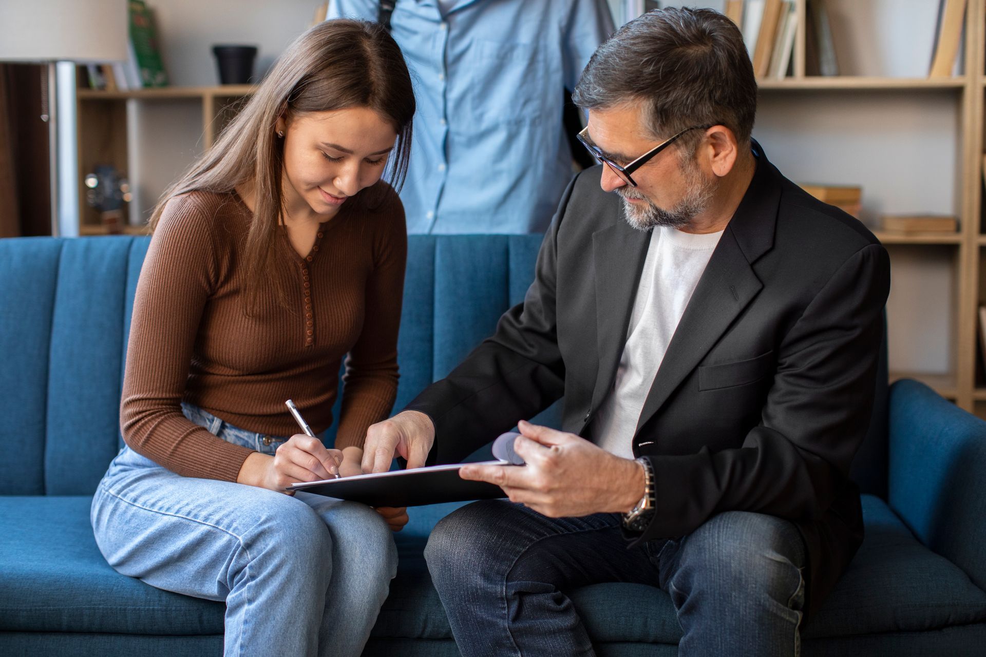 A man and a woman are sitting on a couch signing a document.