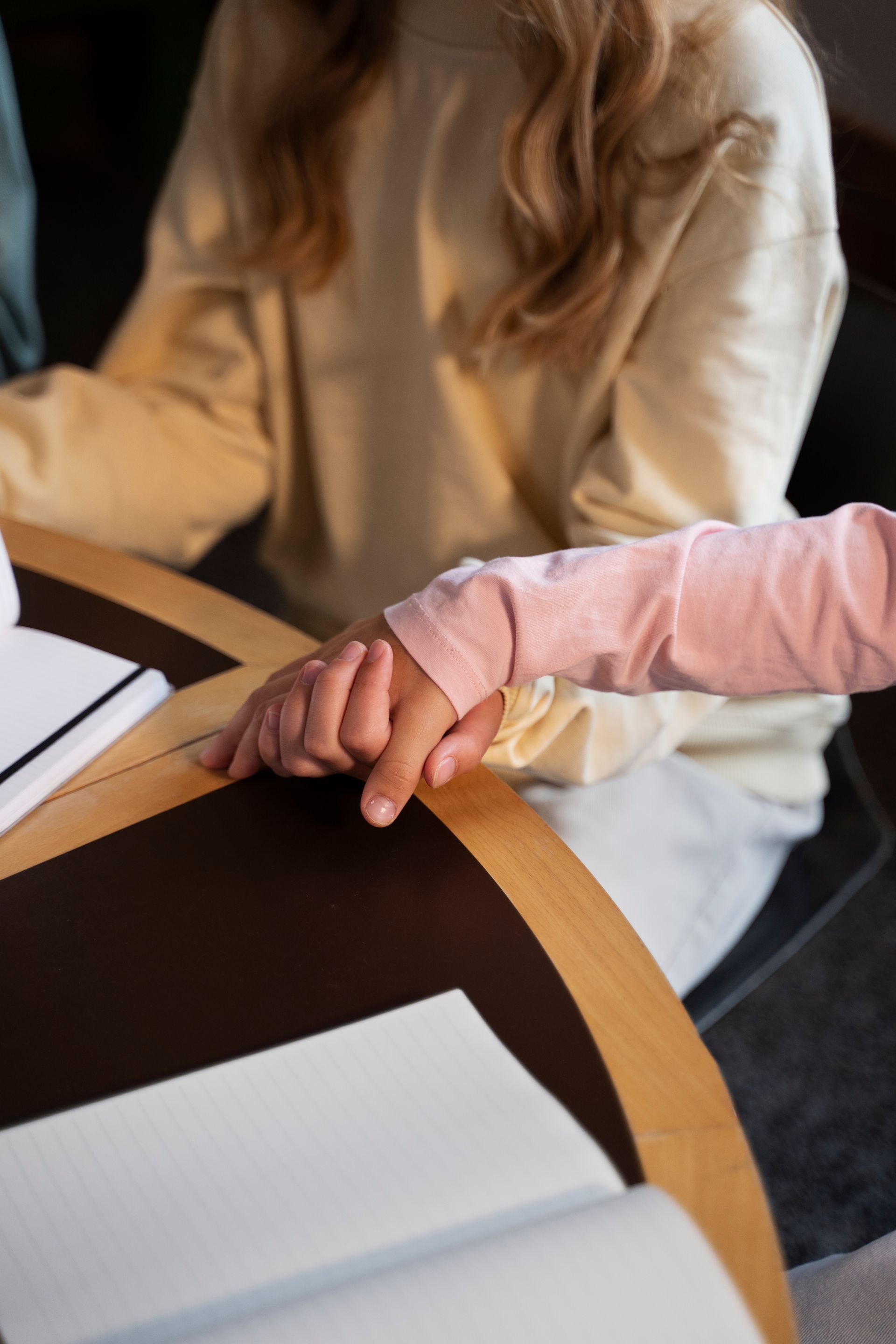 A person is holding another person 's hand while sitting at a table.