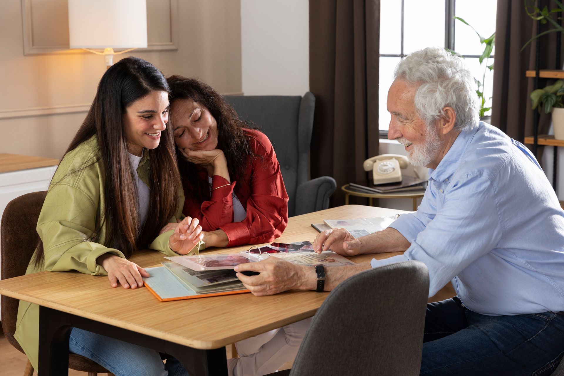 A man and two women are sitting at a table looking at a book.