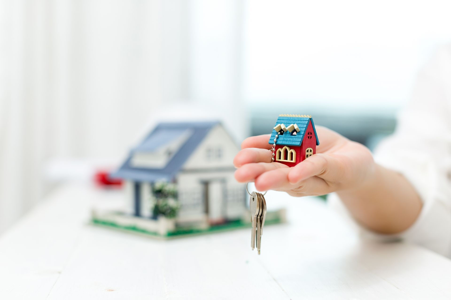 A child is holding a toy house and keys in front of a model house.