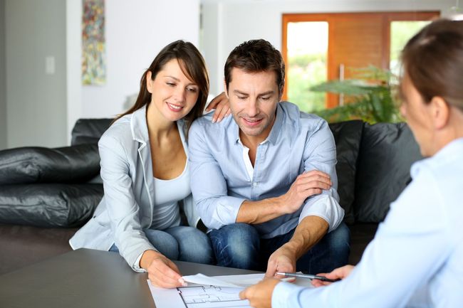 A man and a woman are sitting on a couch talking to a real estate agent.