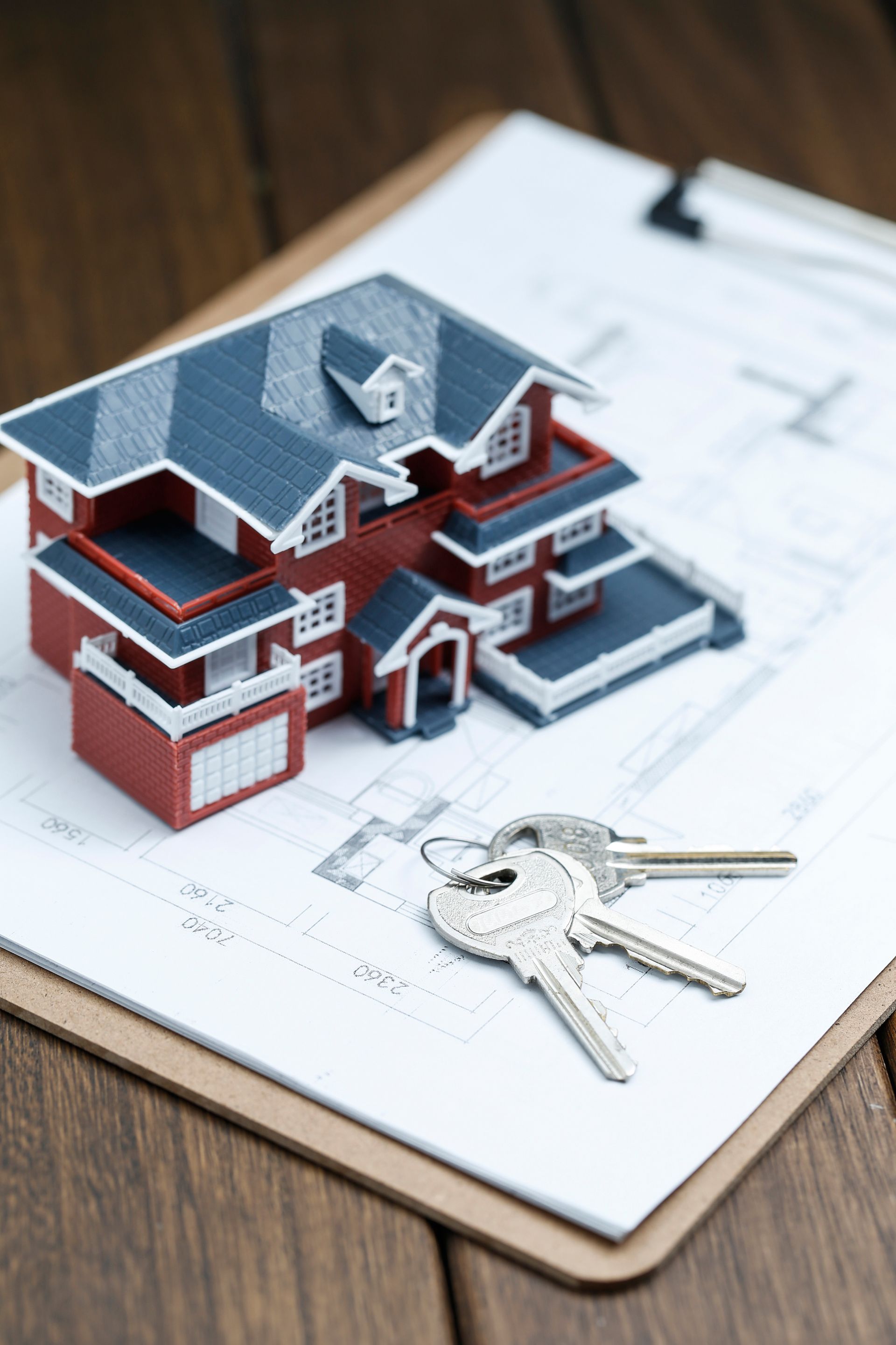 A model house and keys on a clipboard on a wooden table.