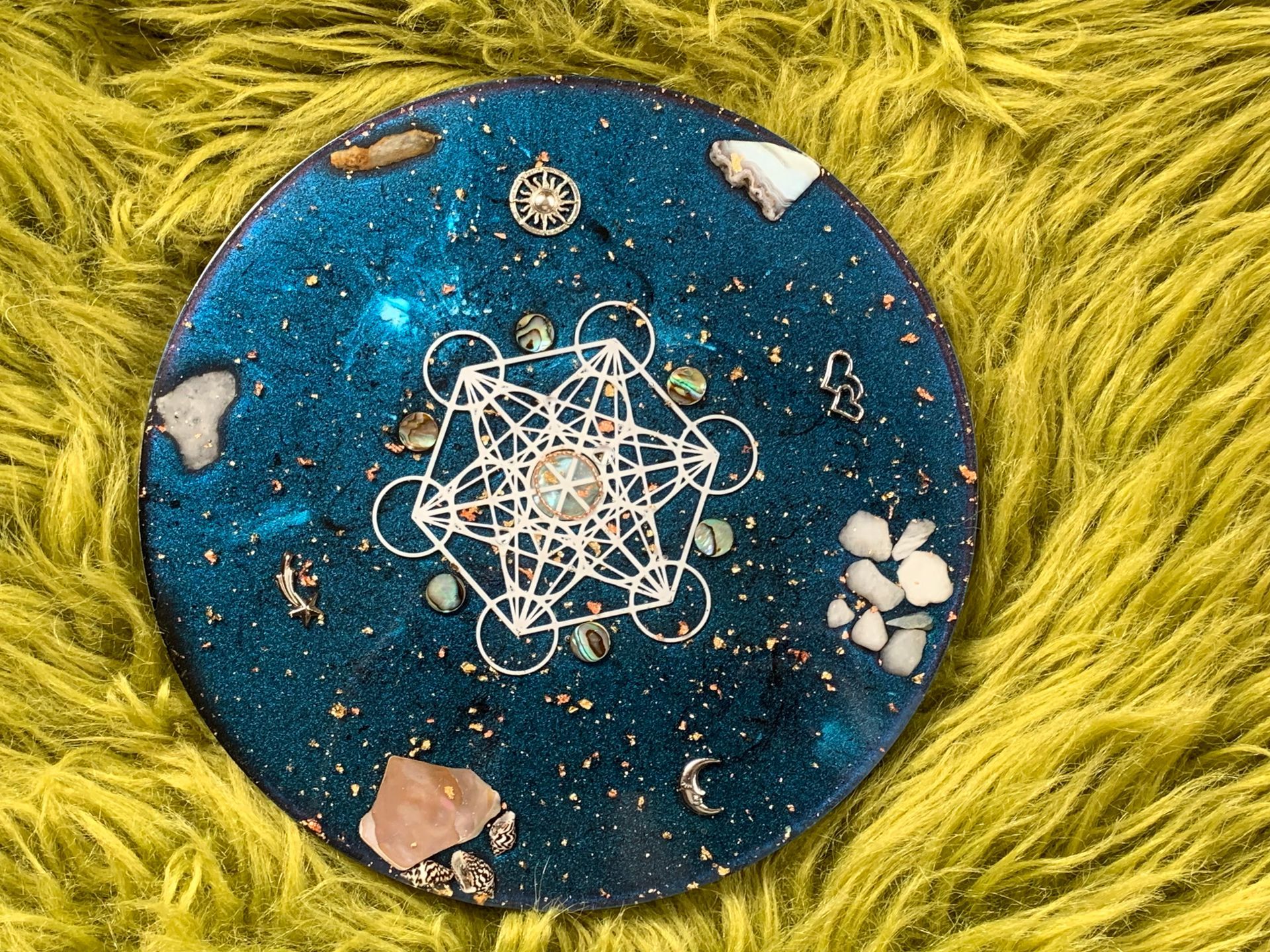 Orgonite. Een blauw bord met een geometrisch patroon erop ligt op een groen, harig oppervlak.