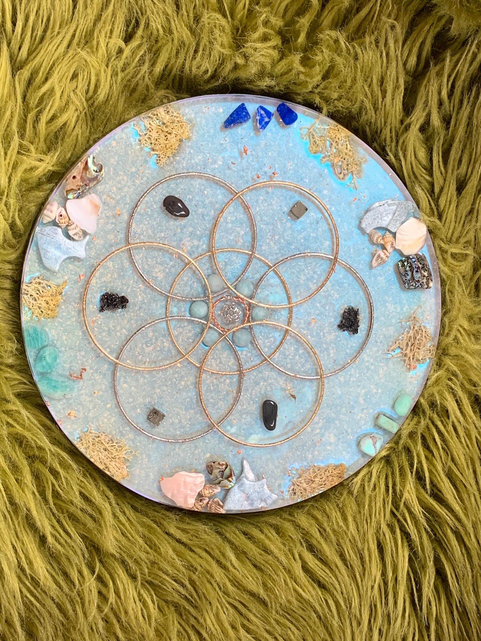 Orgonite. Een cirkel met daarop een levensbloem zit op een groene deken.