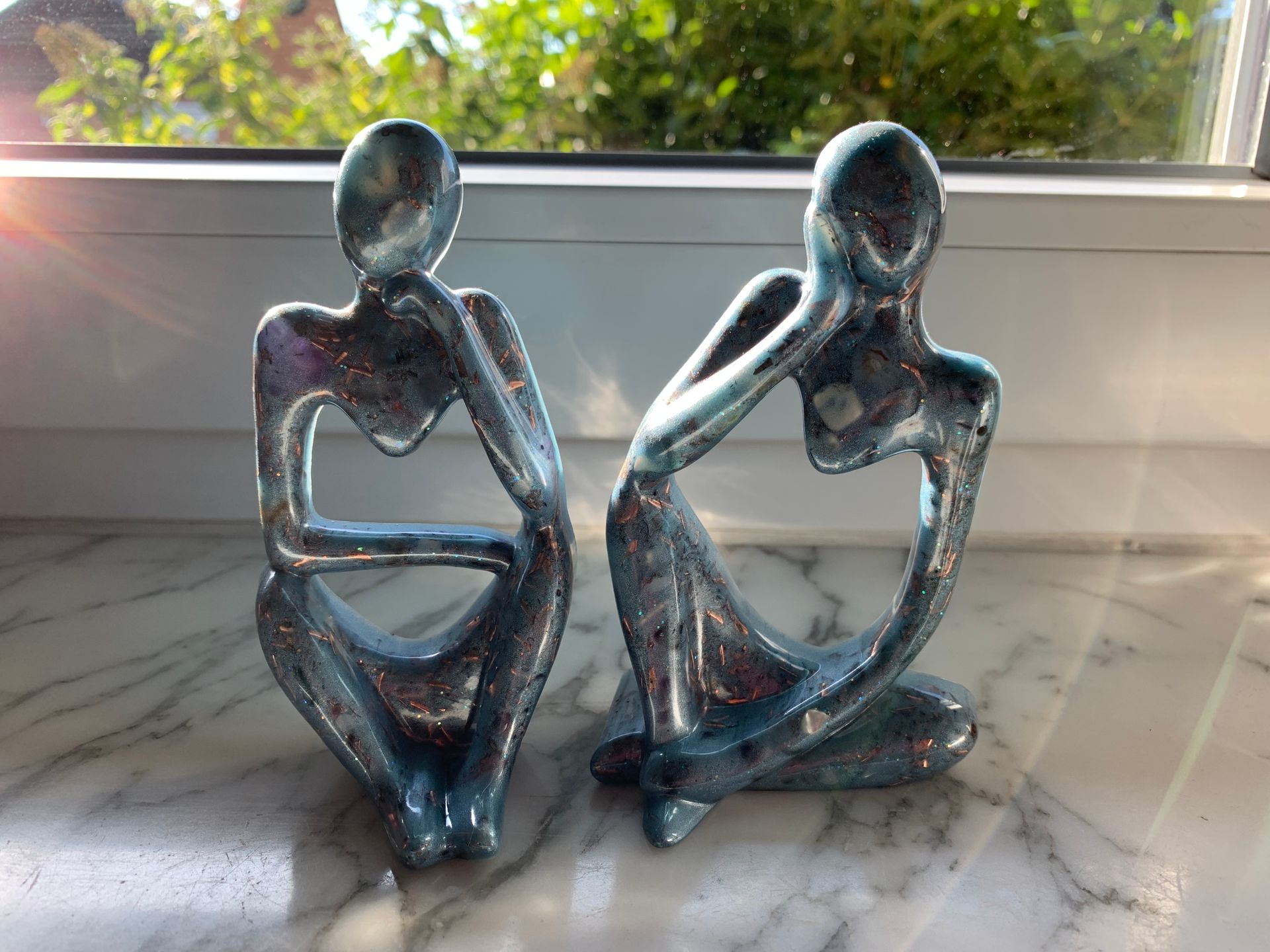 Orgonite. Twee beelden van mensen die naast elkaar op een vensterbank zitten.