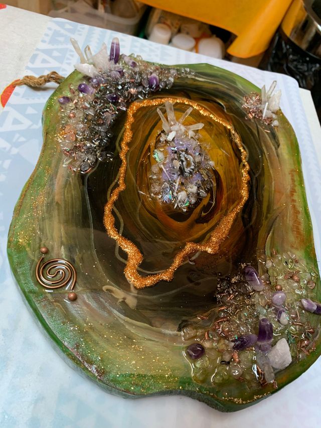 Orgonite. Een groen bord met paarse en gouden versieringen staat op een tafel.
