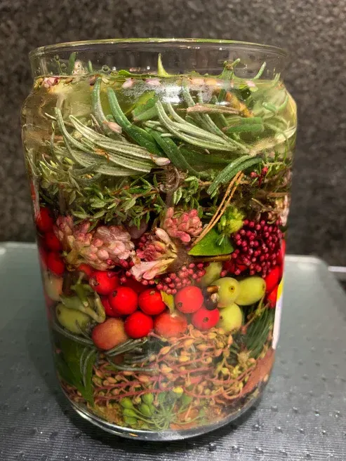 Er staat een glas met fruit en groenten op tafel.