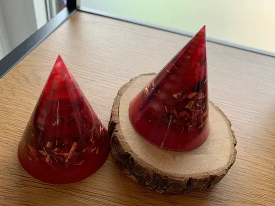 Orgonite. Twee rode kegels liggen op een houten schijf op een tafel.
