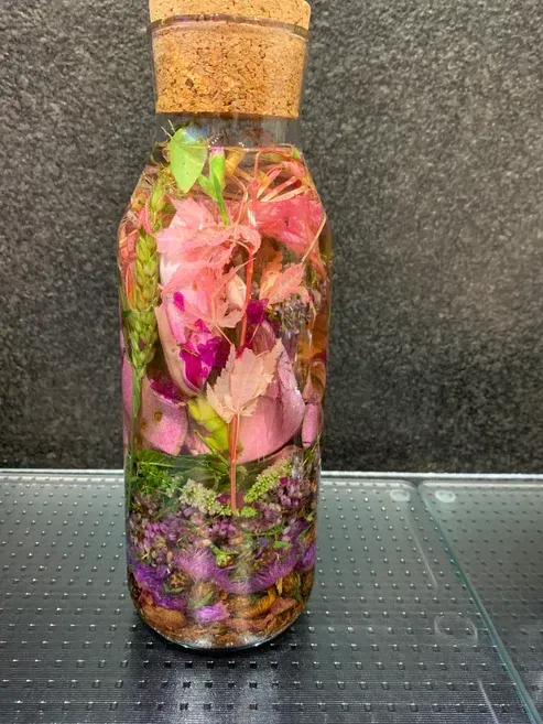 Agua de Florida. Een glazen fles gevuld met bloemen en bladeren op een tafel.