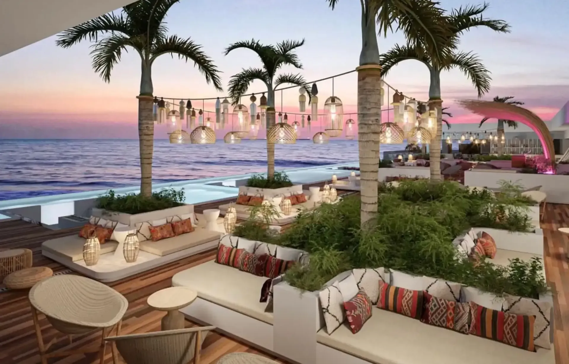 Oceanfront lounge with white sofas, palm trees, string lights, and a pink sculpture at sunset.