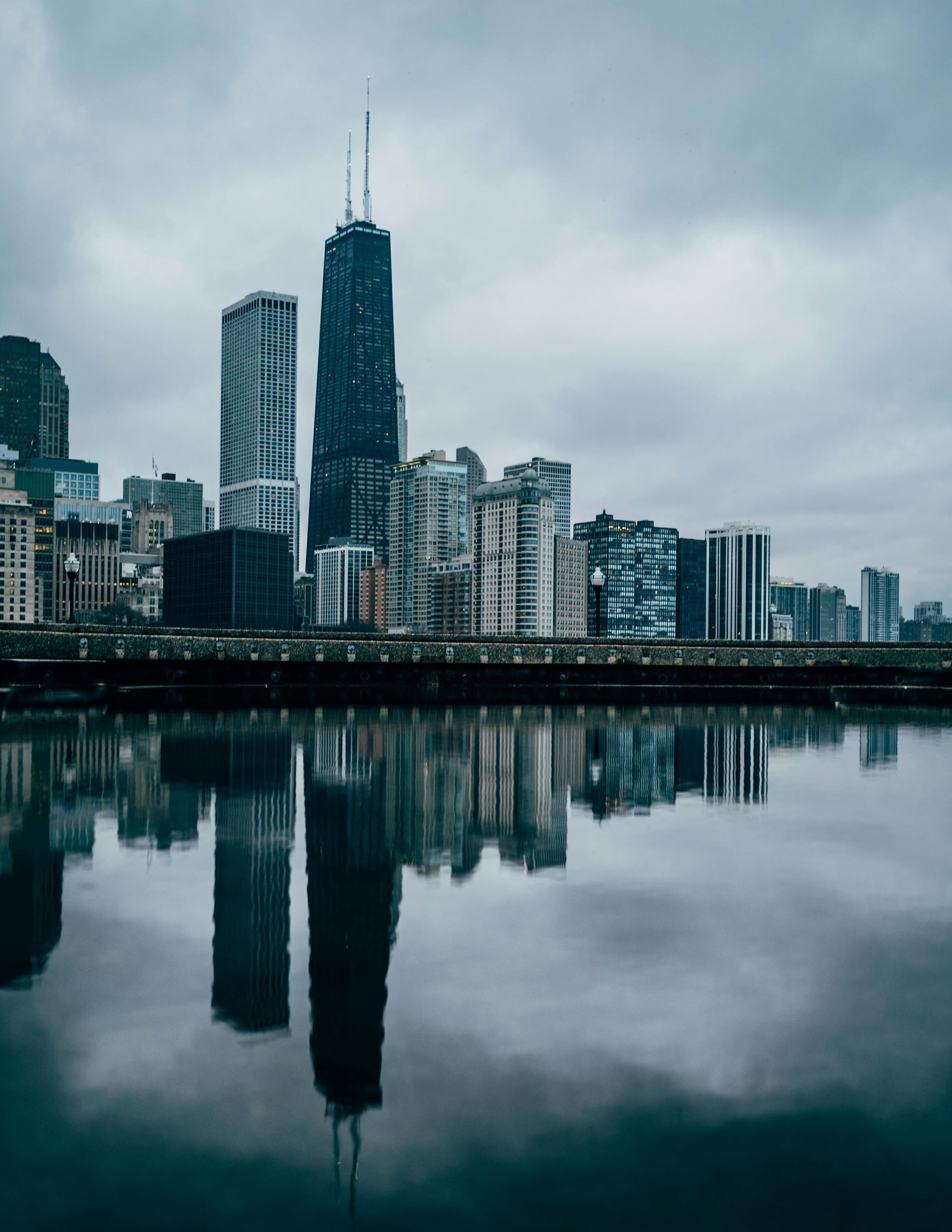 Chicago skyline reflected in water on a cloudy day. Skyscrapers dominate the view.