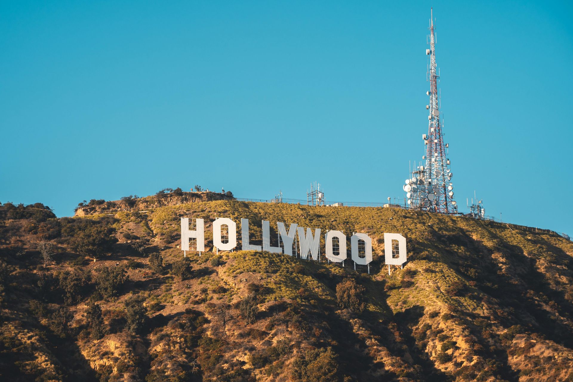 Hollywood sign on a hillside with a communications tower, under a clear blue sky.