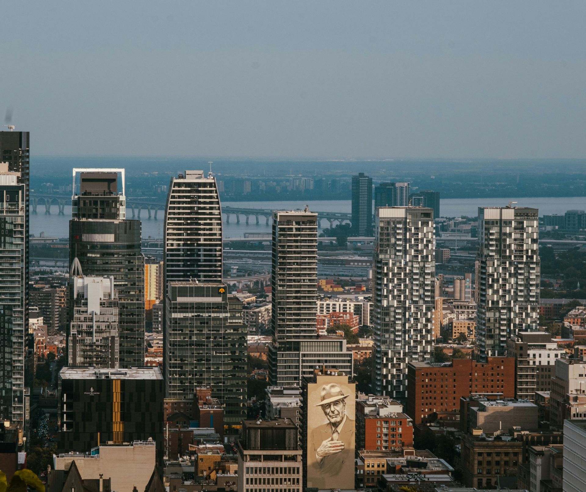 City skyline with skyscrapers; a bridge and body of water in the background. Buildings range in height and style.