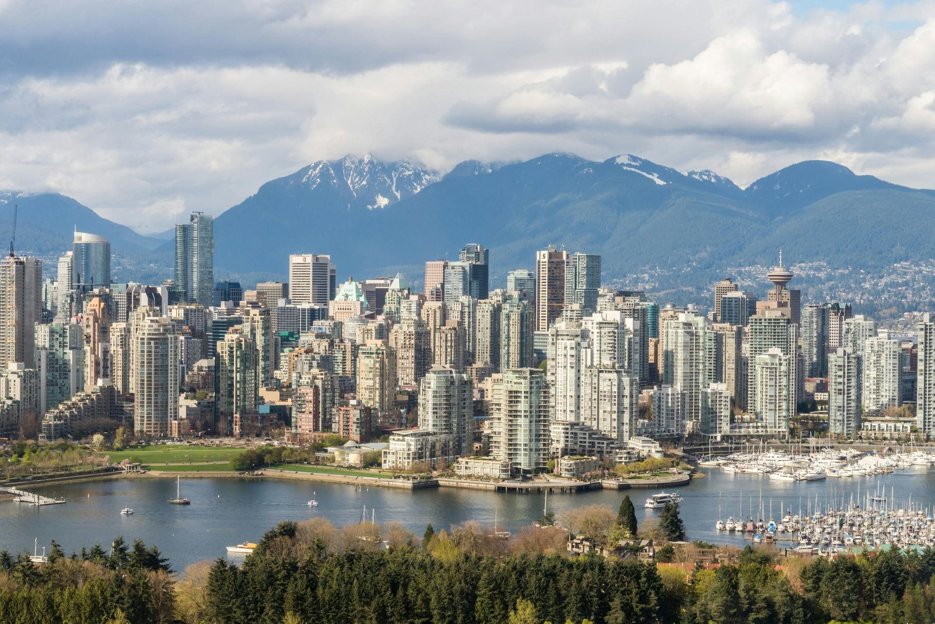 Vancouver skyline with mountains in the background, a harbor in the foreground, and a few clouds overhead.
