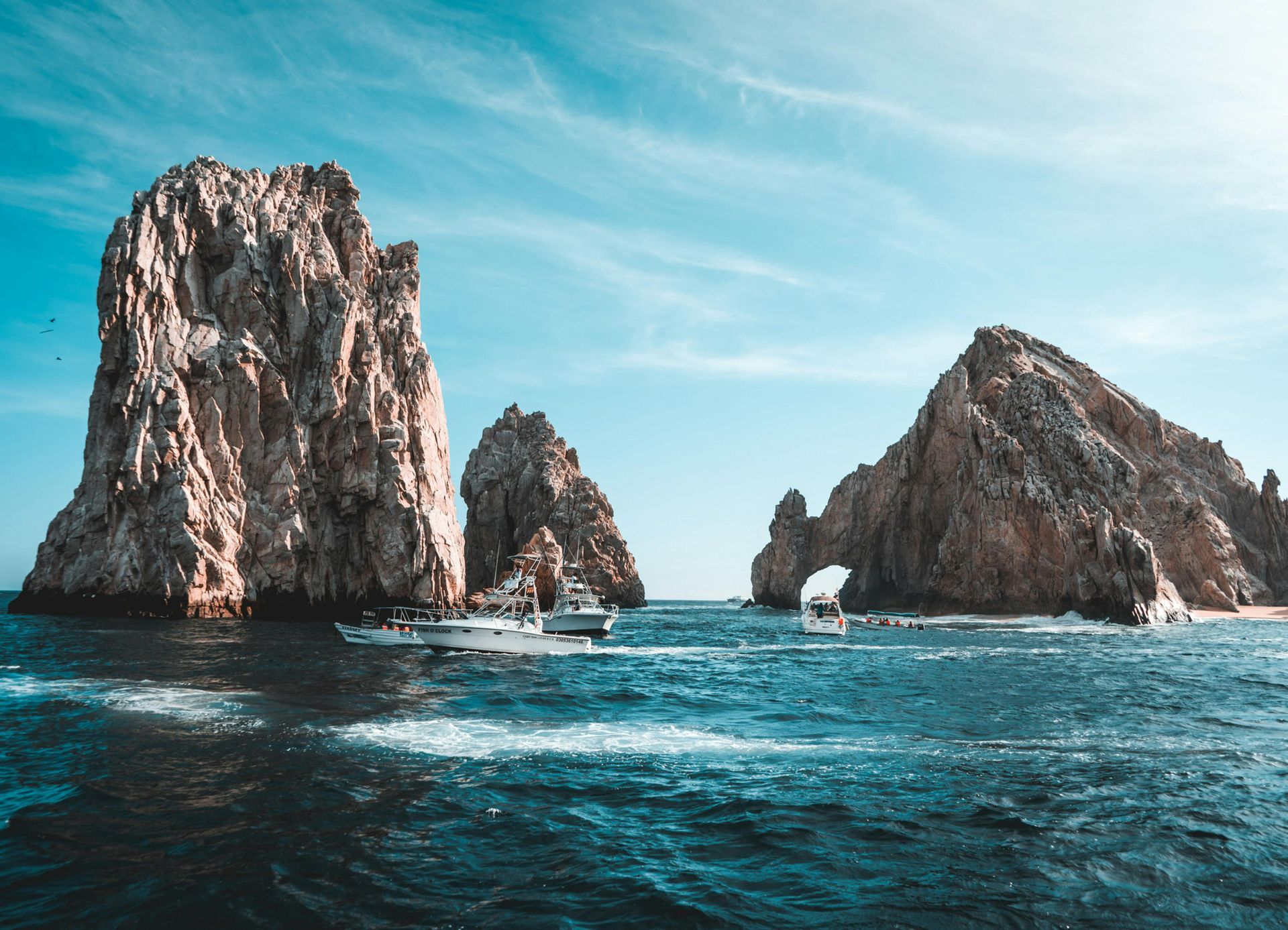 Rocky cliffs jutting from ocean; boats sail beneath blue sky.