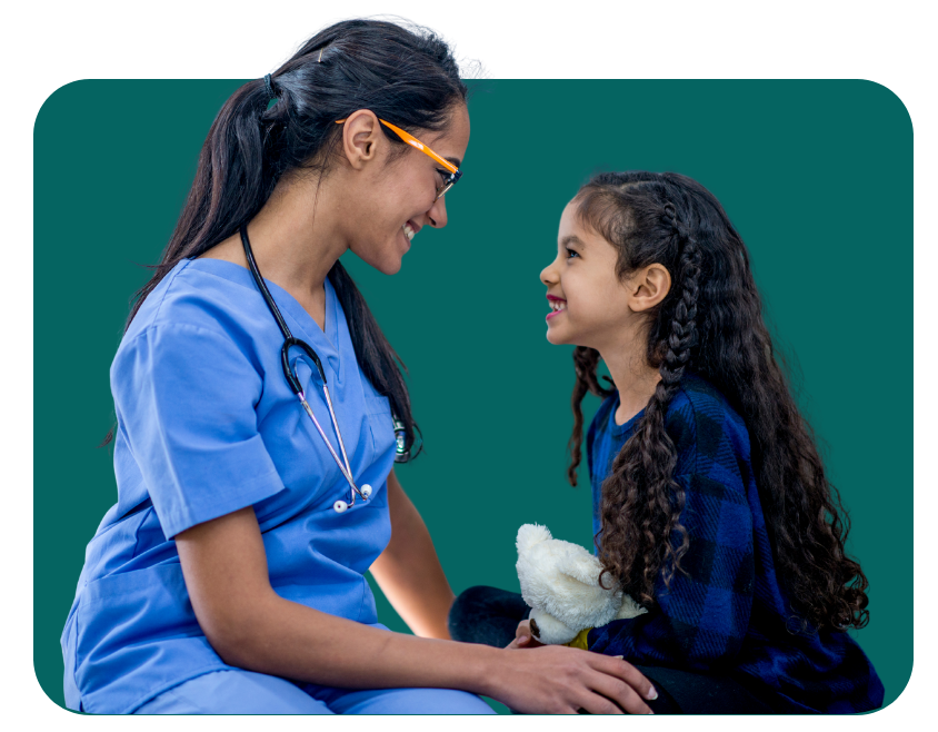 Nurse smiling at a young girl, both looking at each other. They are indoors in front of a green background.