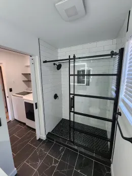 Modern bathroom with black and white tile, shower with sliding glass door, and black fixtures.