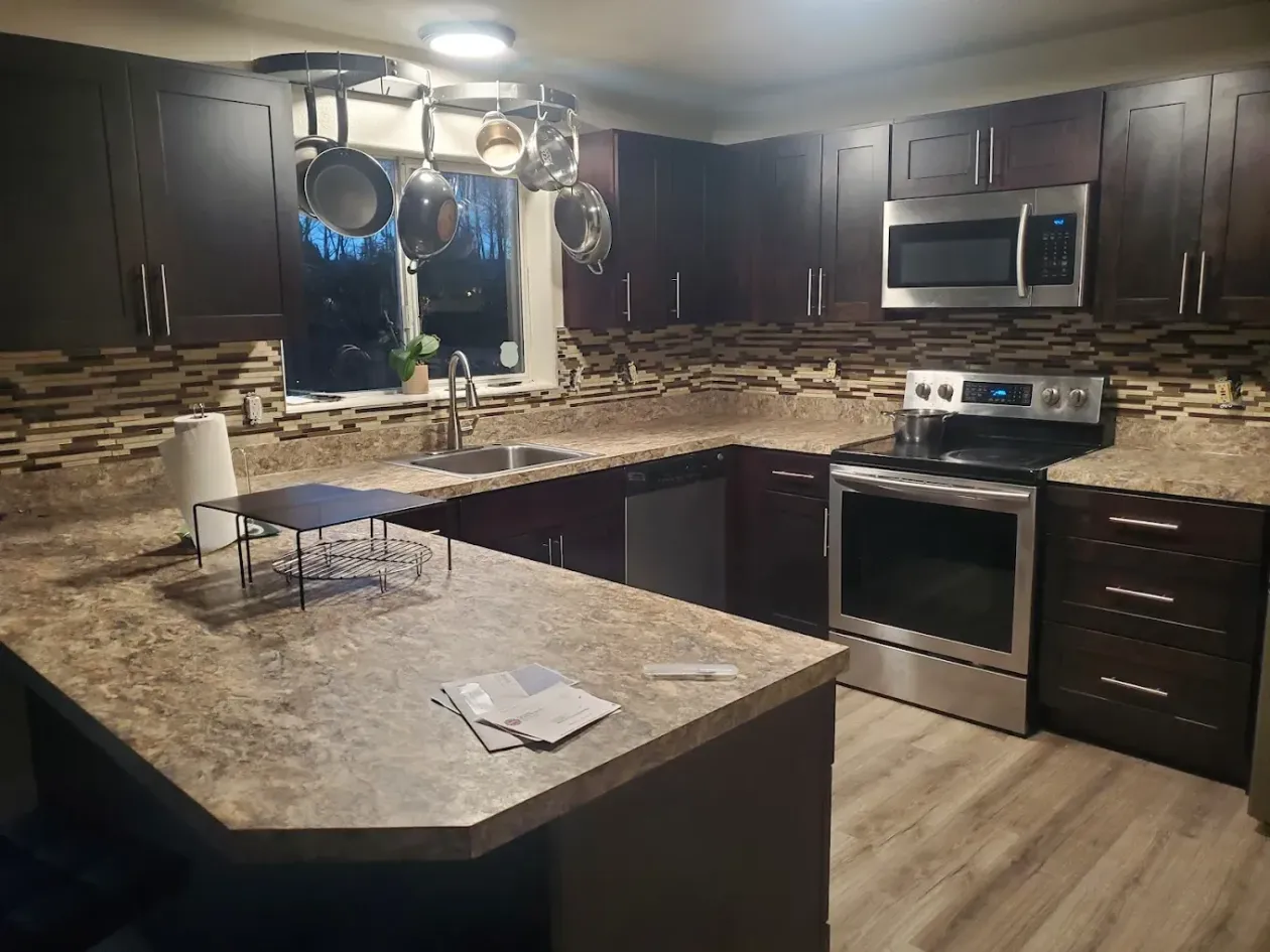 Dark kitchen with brown cabinets, stainless steel appliances, beige countertops, and a hanging pot rack.